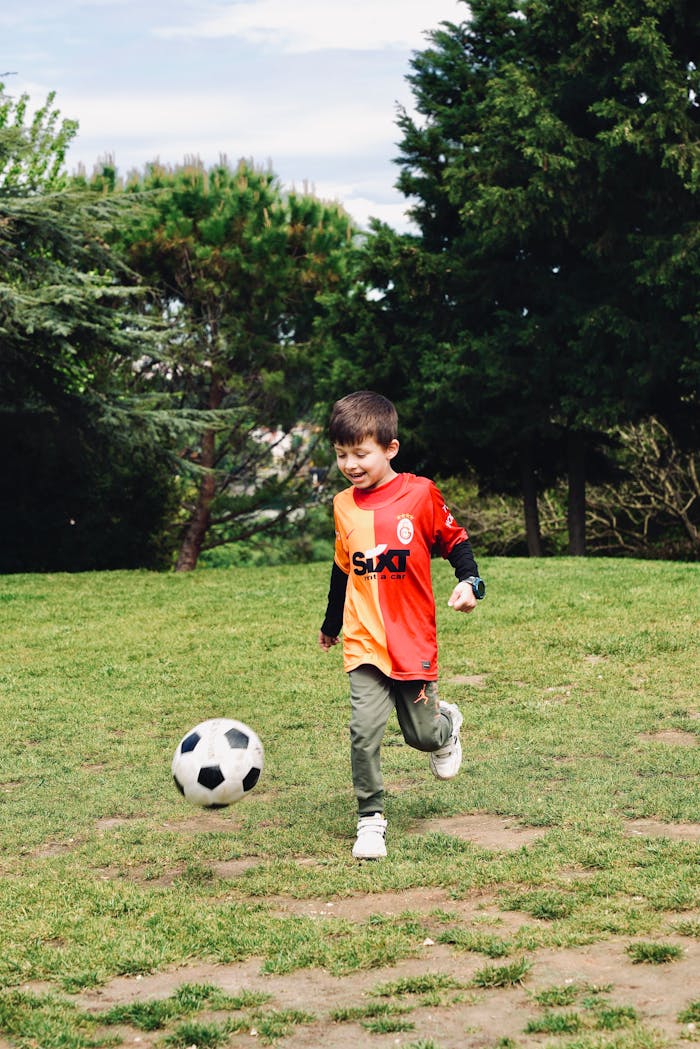 A cheerful child playing soccer in a lush green park, enjoying a sunny outdoor day.