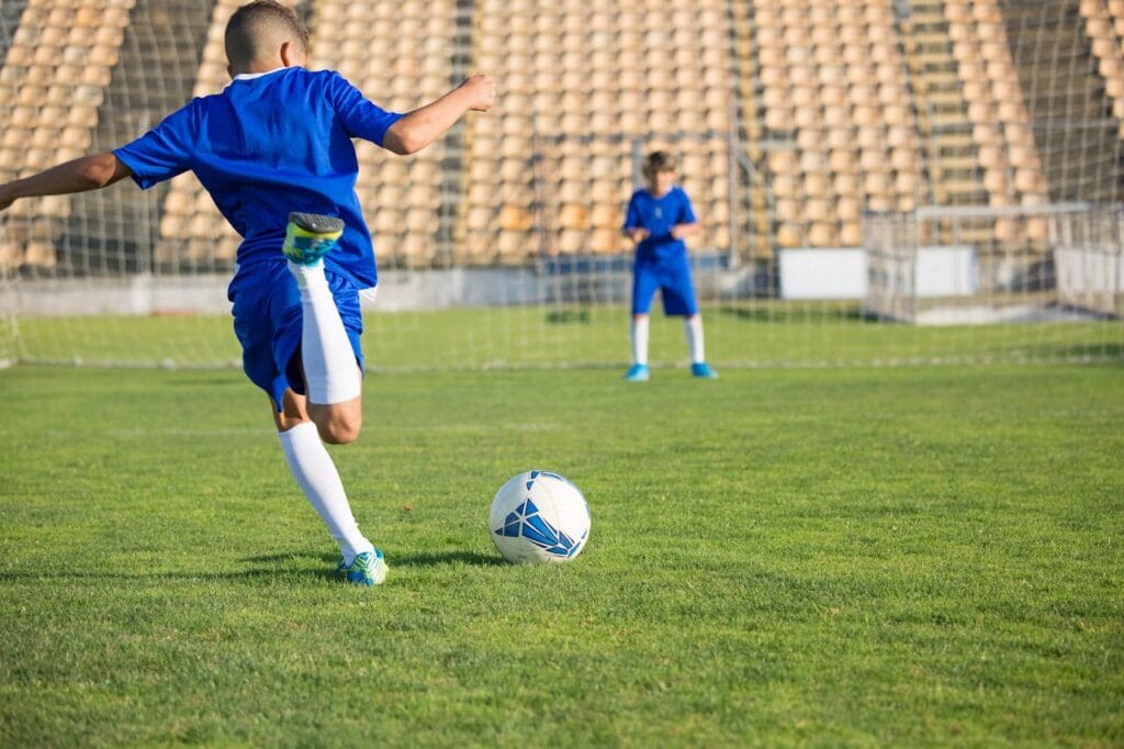pexels-photo-8941646 Two boys in blue uniforms practice soccer on a sunny field, focusing on the ball.