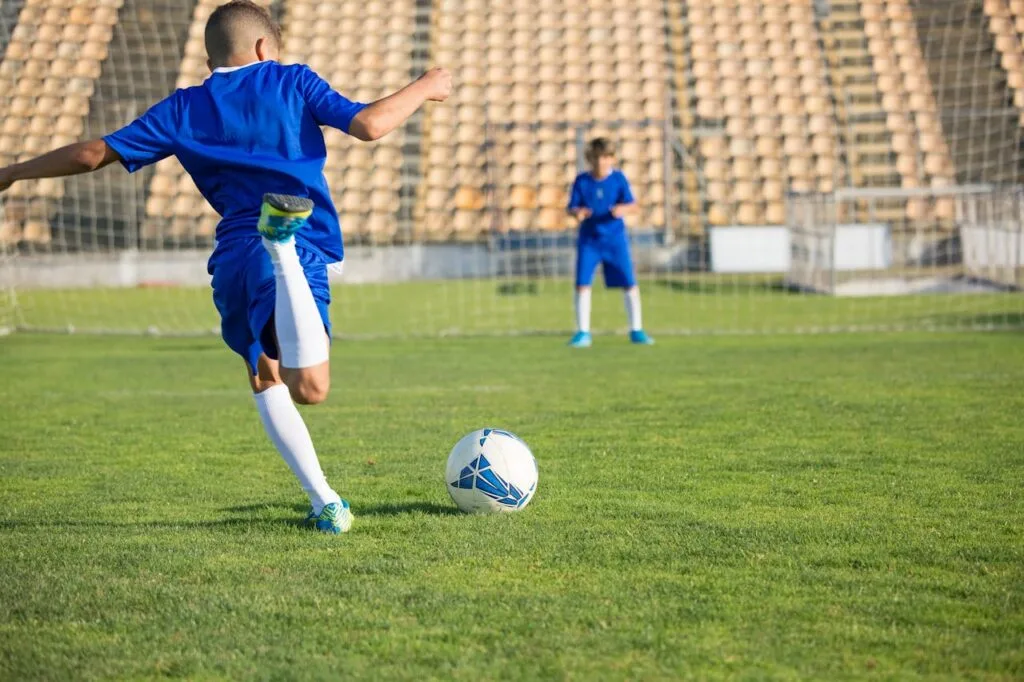 Two boys in blue uniforms practice soccer on a sunny field, focusing on the ball.